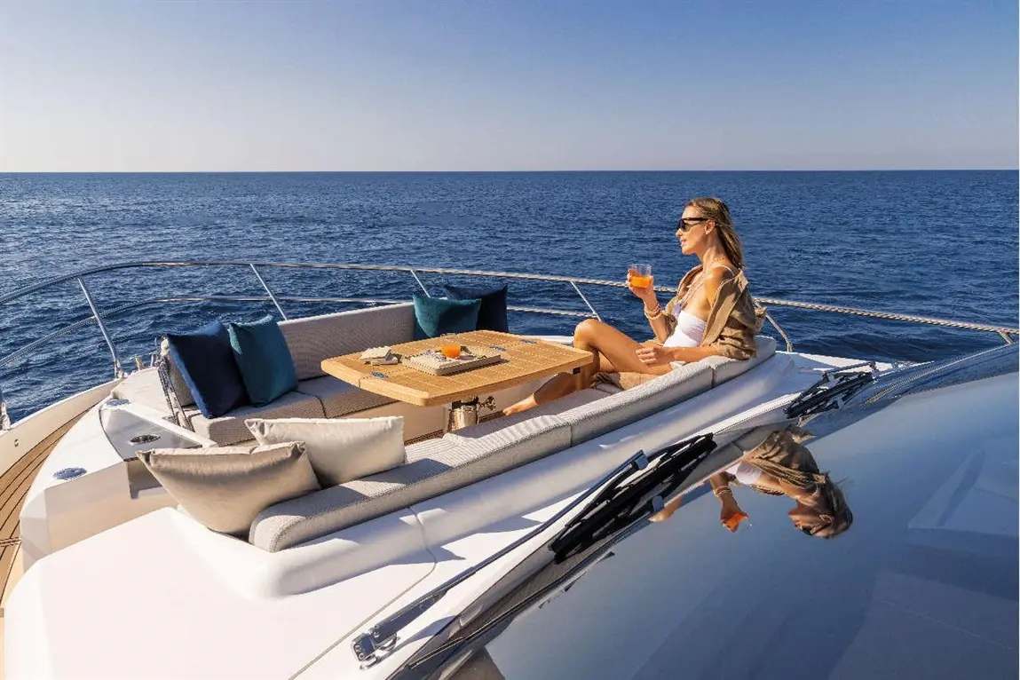 Woman relaxing on a yacht, holding a drink, with a table set on the deck and a clear view of the ocean.